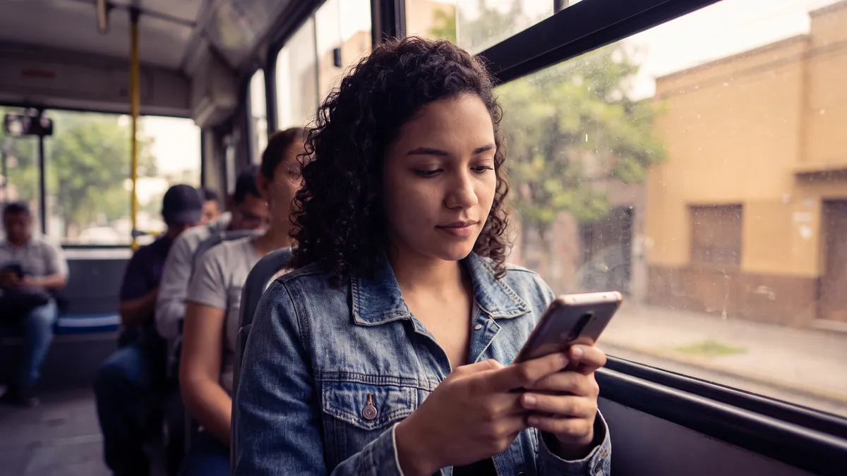 A young woman on a city bus taps an ad on her phone that opens a chat with a store